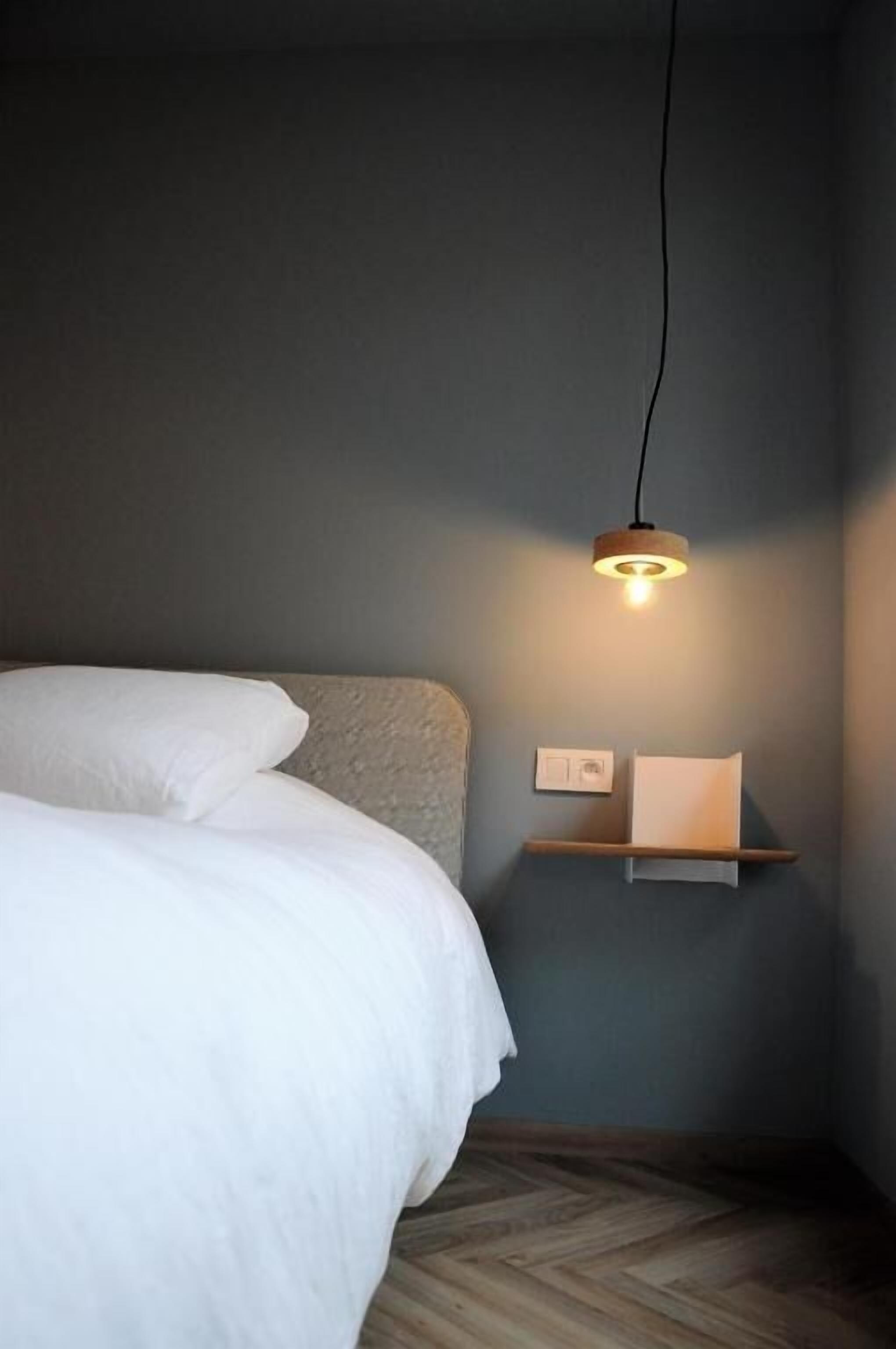Une chambre à coucher avec un lit, une étagère fixée au mur et un luminaire suspendu.
