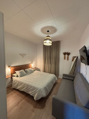 Ein modernes Schlafzimmer mit Bett, Sofa, Fernseher und einer Kronleuchter.