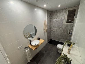 Ein modernes Badezimmer mit einem runden Spiegel, einem Holzlager, einer Toilette und einer Duschkabine.