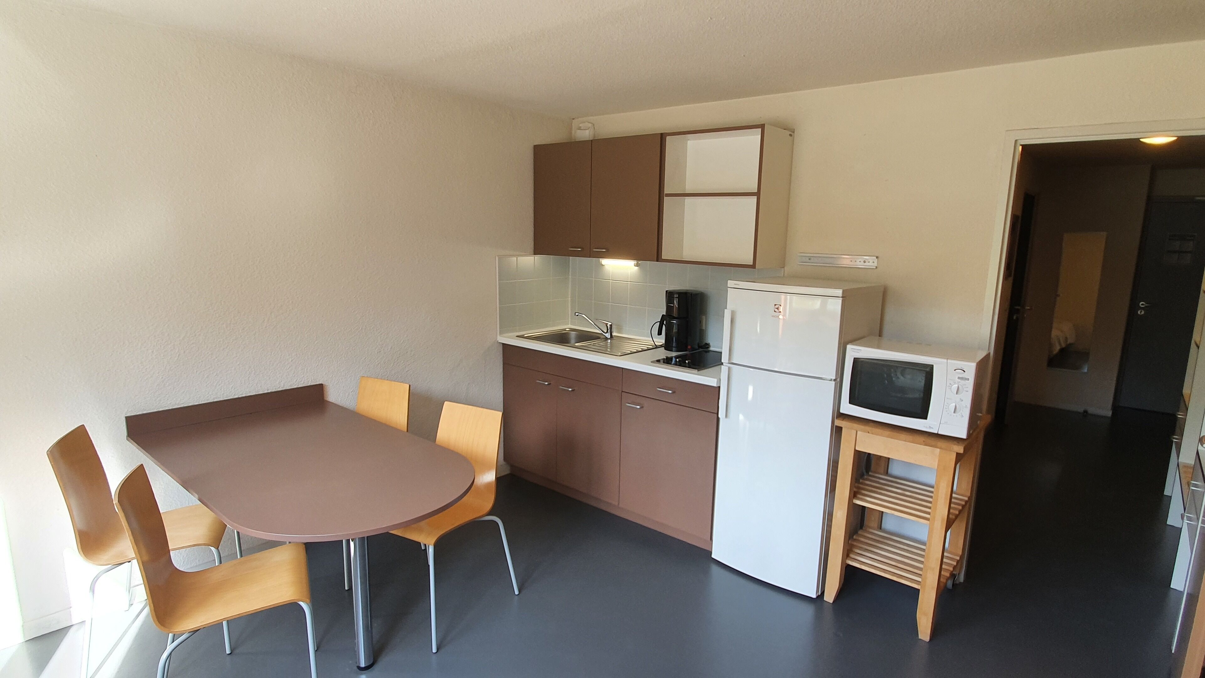 Eine kleine Küchenzeile mit Spüle, Kaffeemaschine, Mikrowelle und Kühlschrank. Ein Esstisch mit vier Stühlen steht daneben.