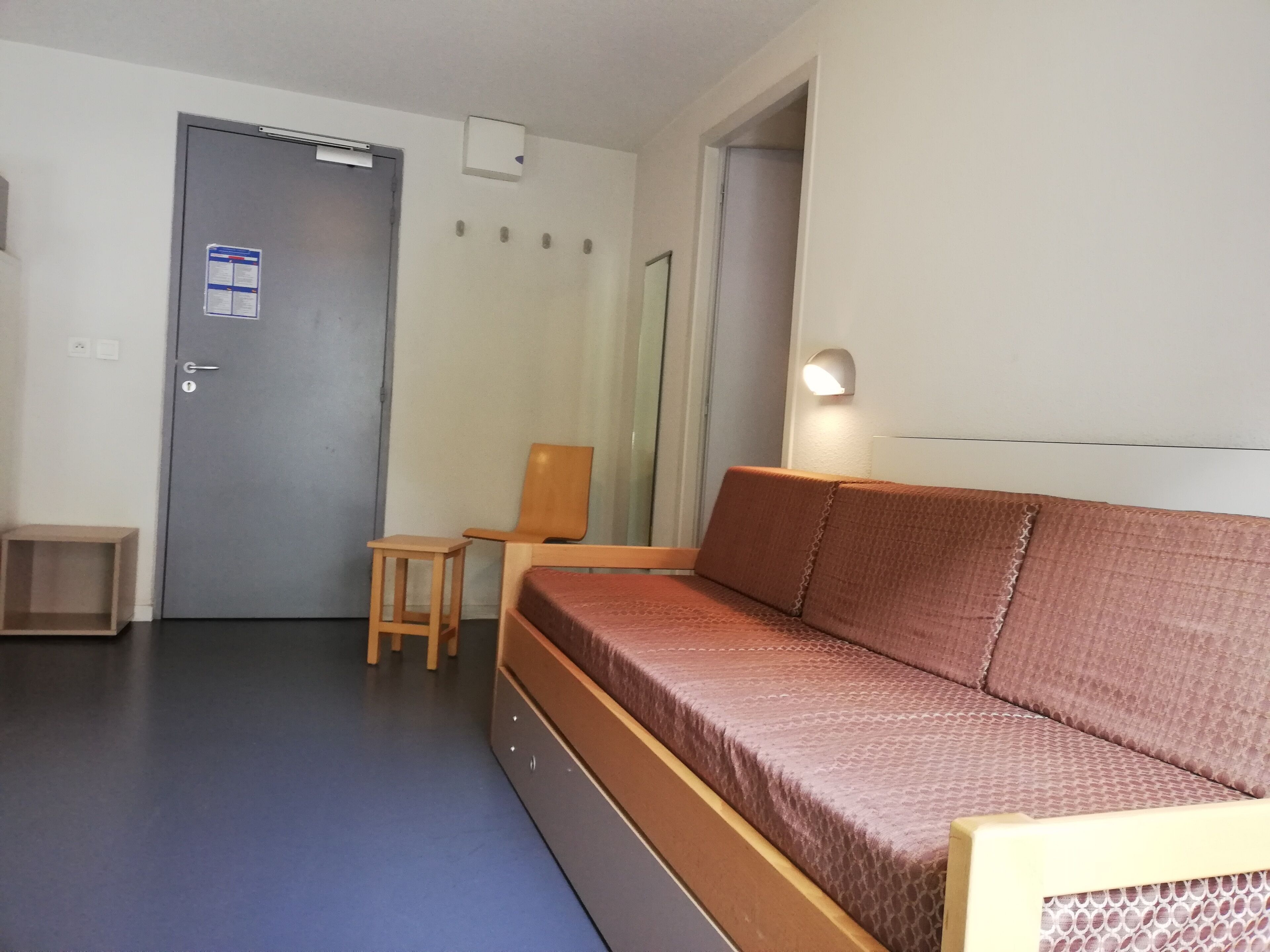 A room with a grey door, a wooden chair, a brown sofa, and a small wooden table.