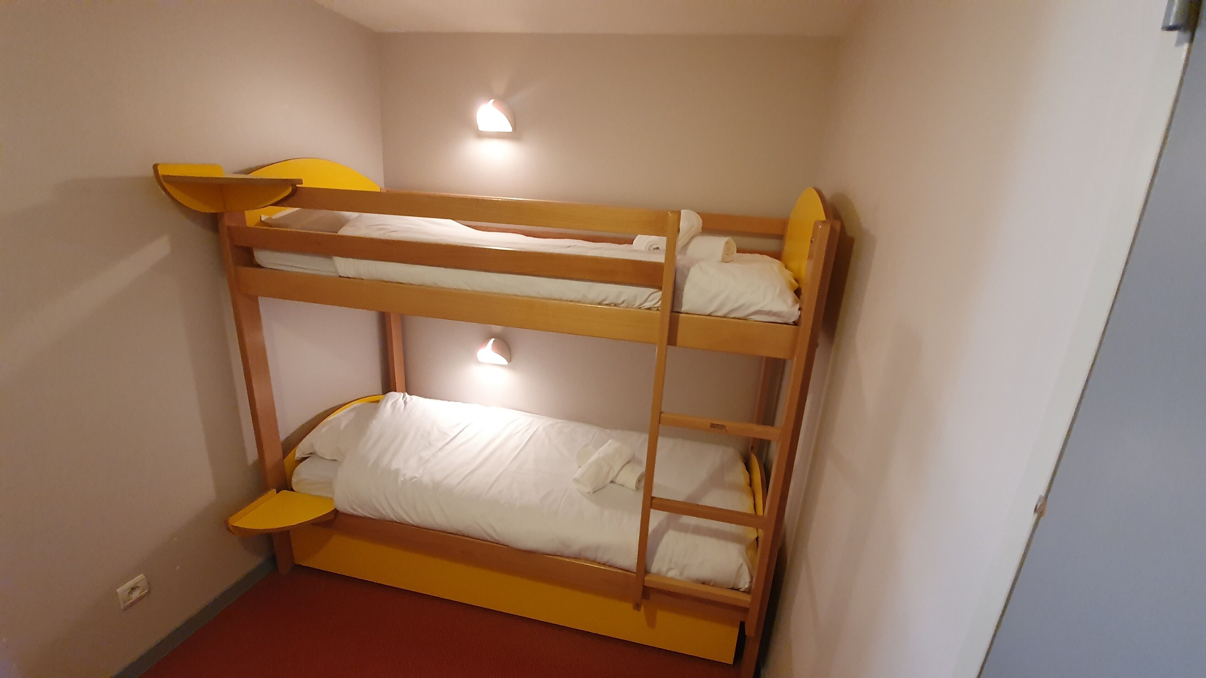 A bunk bed room with two levels, each with a pillow and a small bedside table.