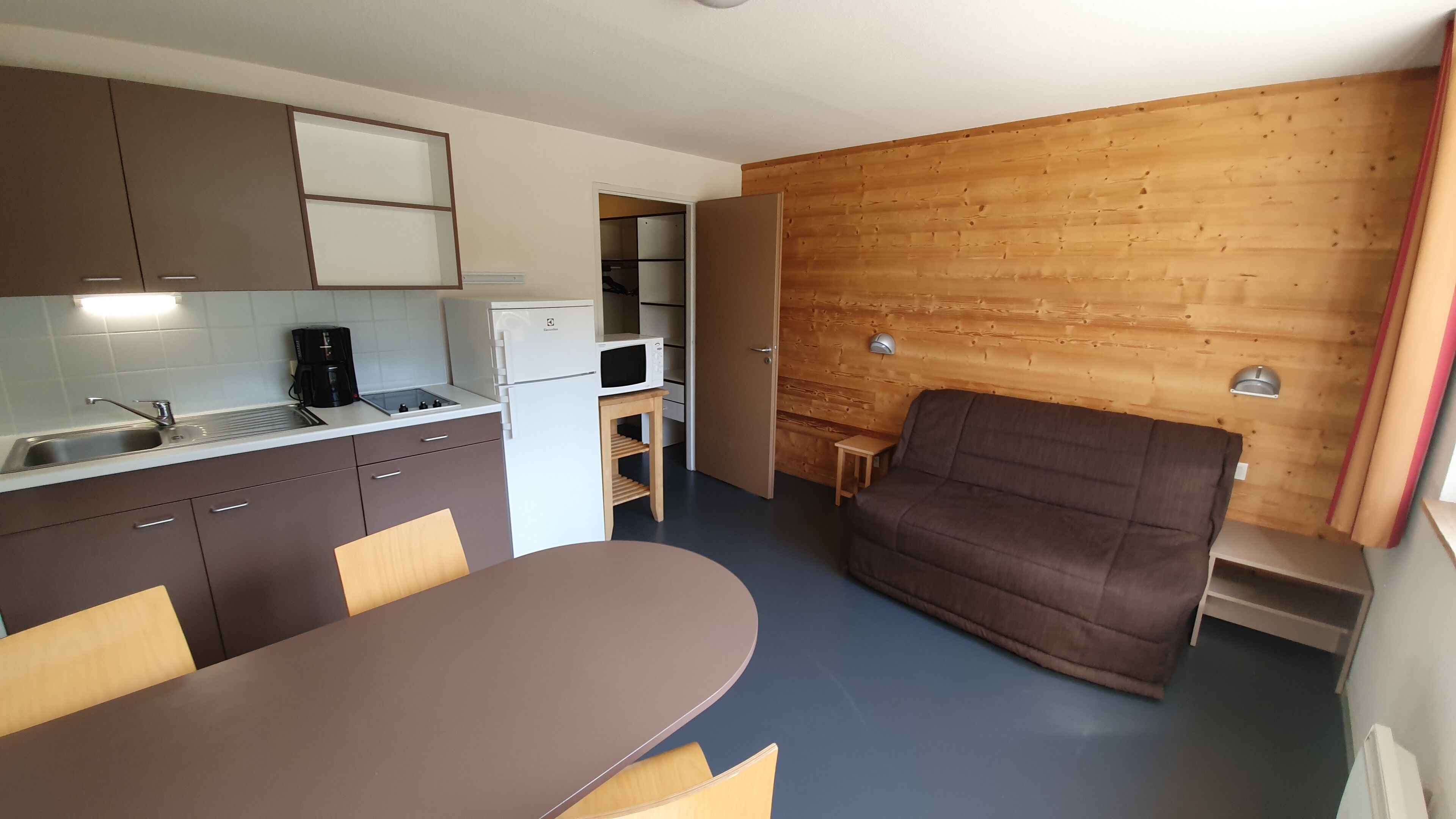 A compact kitchen with a dining area, a sofa, and a wooden wall.