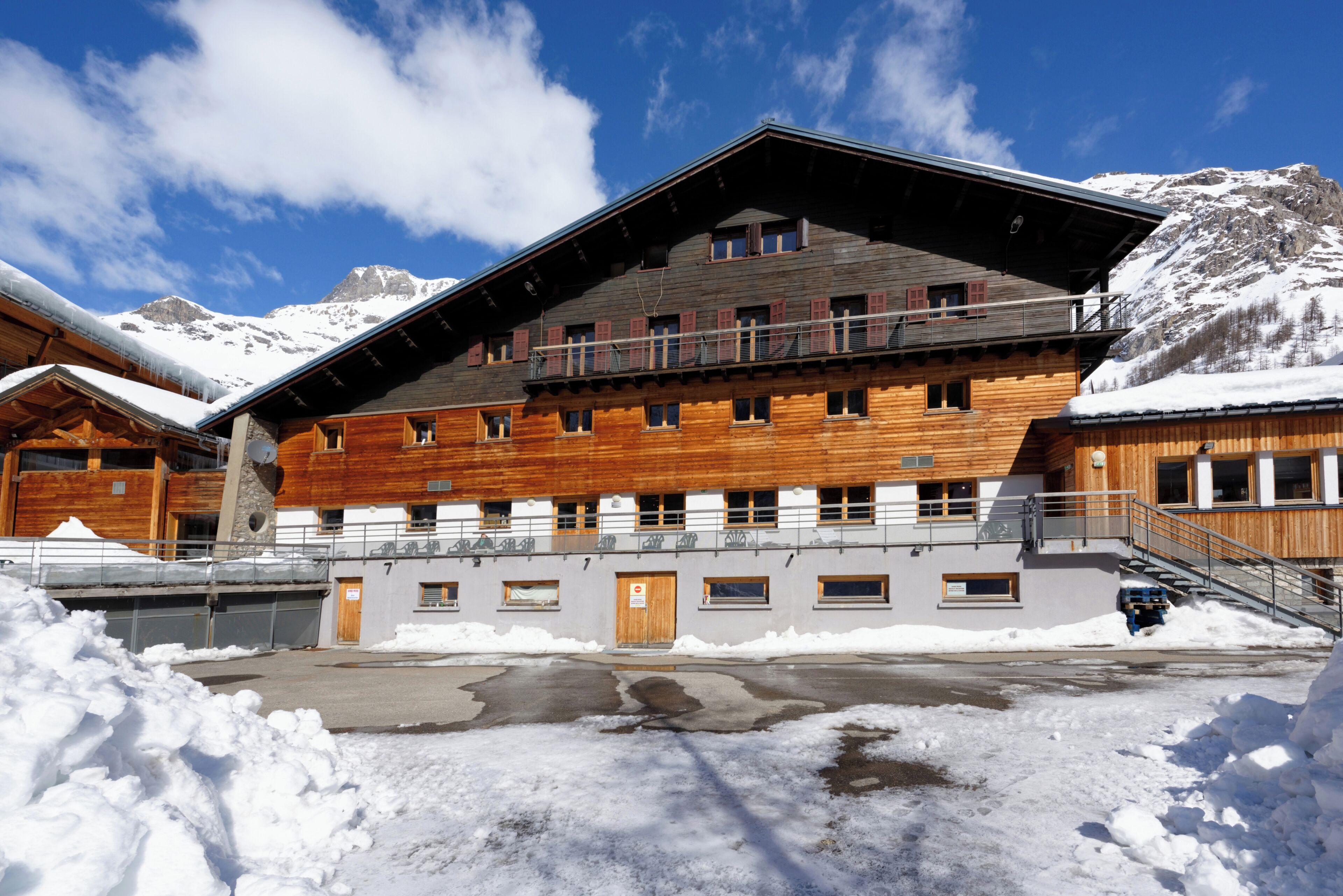 A wooden building with multiple windows and balconies, surrounded by snow and mountains.