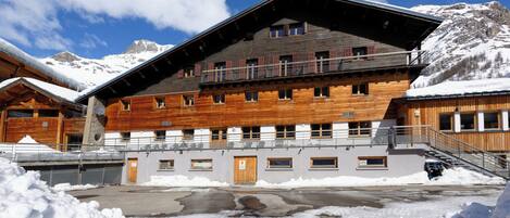 A wooden building with multiple windows and balconies, surrounded by snow and mountains.