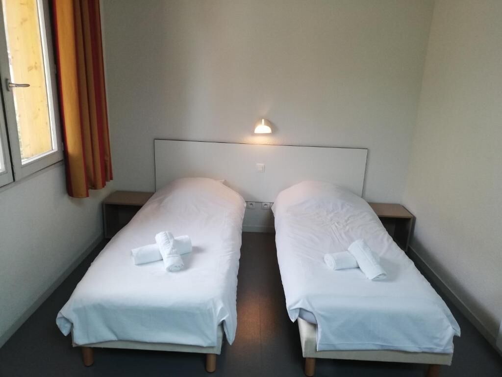 Ein Doppelzimmer mit zwei Einzelbetten, einem Nachttisch, einer Wandleuchte und einem Fenster mit Vorhängen.