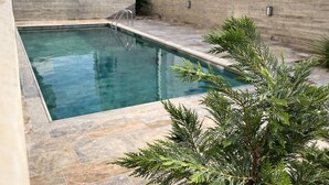 A rectangular pool with a clear blue water surface, surrounded by a stone patio. - Oni Residence Apartment (Limassol)