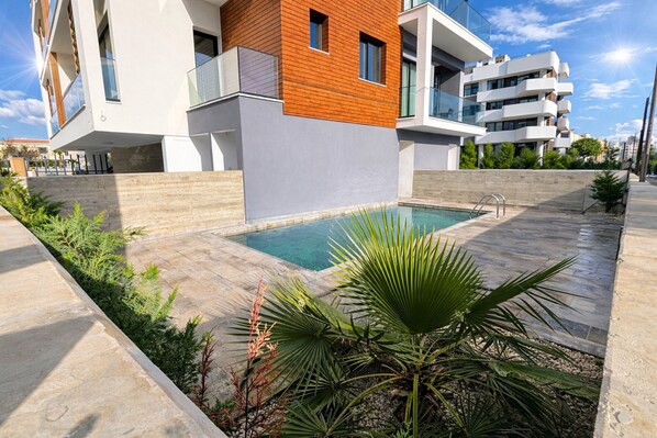 A modern building with a swimming pool, surrounded by plants and a clear sky. - Oni Residence Apartment (Limassol)