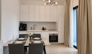 Une cuisine moderne avec des meubles blancs, une table à manger dressée pour deux personnes et une grande fenêtre agrémentée de rideaux.