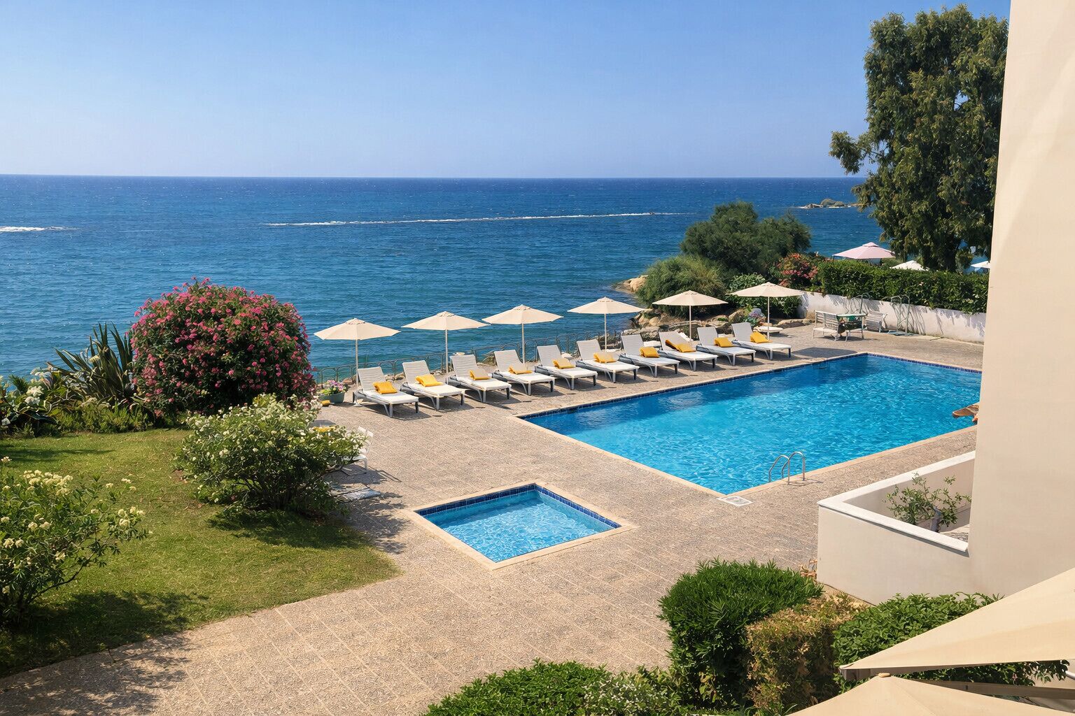 Una piscina con sillones y sombrillas, rodeada de vegetación y con vista al mar.