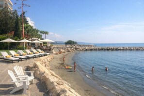 A beach with lounge chairs, umbrellas, and a rocky shoreline. - Gulf Beach Apartment (Limassol)