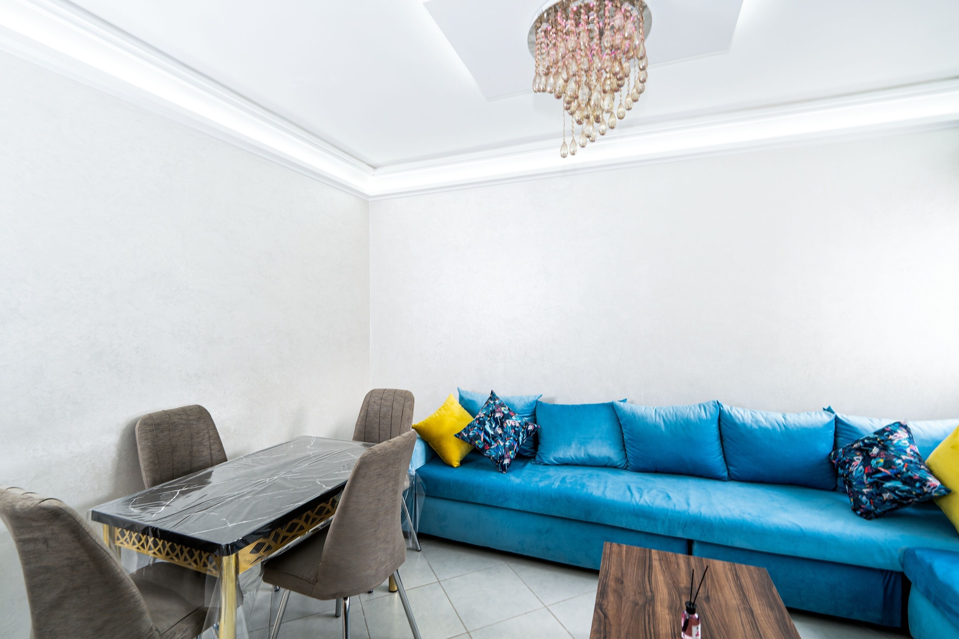A modern living room with a blue sofa, a dining table, and a chandelier.