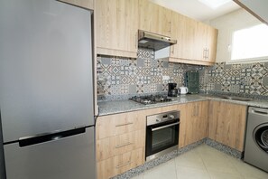 Uma cozinha com armários de madeira, uma geladeira de aço inoxidável, forno embutido e uma máquina de lavar.