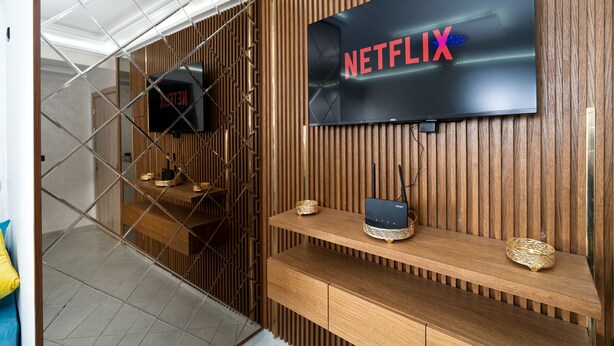 Ein modernes Zimmer mit Holzwandverkleidung, einem Netflix-Fernseher, einem Router und einer kleinen Ablagefläche mit Dekoration.