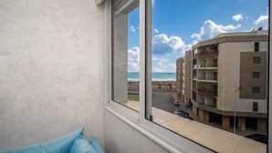 Ein Zimmer mit großem Fenster, Blick auf ein Gebäude und einen Strand.