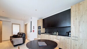 A modern kitchen with dark cabinets, a round dining table, and a massage chair. - Stunning Penthouse near St. Julian's w/ Pool (Is-Swieqi)