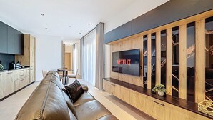 A modern living room with a leather sofa, a TV mounted on a wooden wall, and a kitchen area in the background. - Stunning Penthouse near St. Julian's w/ Pool (Is-Swieqi)