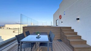 A rooftop terrace with a table and chairs, a small plant, and a red lifebuoy on the wall. - Stunning Penthouse near St. Julian's w/ Pool (Is-Swieqi)