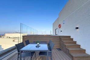 Eine Dachterrasse mit Tisch und Stühlen, einer kleinen Pflanze und einem roten Rettungsring an der Wand.