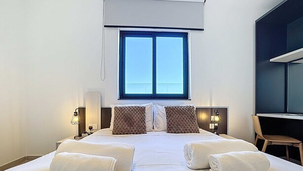 A hotel room with a large bed, two pillows, a window, a desk, and a chair. - Stunning Penthouse near St. Julian's w/ Pool (Is-Swieqi)