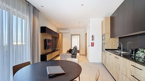 A modern kitchen with dark cabinets, a dining area with a table and chairs, and a living area with a sofa and TV. - Stunning Penthouse near St. Julian's w/ Pool (Is-Swieqi)