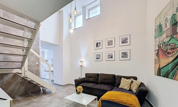 A modern living room with a staircase, a sofa, a coffee table, and a wall with framed pictures. - Historic Malta Home with Rare Indoor Cave Pool (Il-Mellieħa)