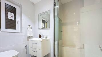 Un baño con lavamanos blanco, espejo, toallero y zona de ducha.