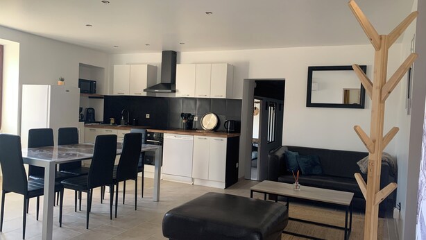 Une cuisine moderne avec des meubles blancs, une cuisinière noire et un coin repas comprenant une table et des chaises.