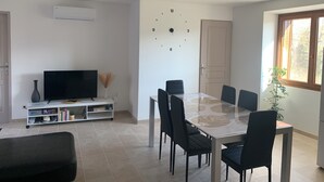 Un salon moderne comprenant un téléviseur, une bibliothèque, une table à manger, des chaises et une horloge murale.