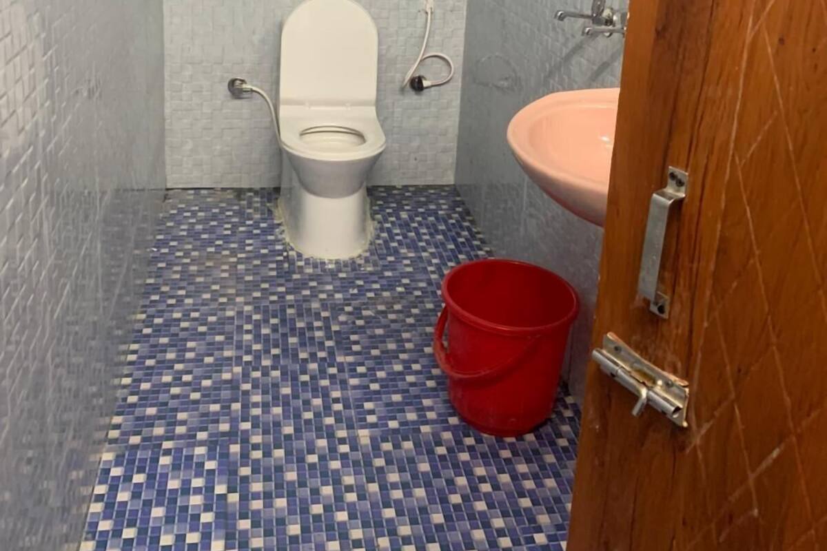A bathroom with a tiled floor, a toilet, a sink, and a red bucket.