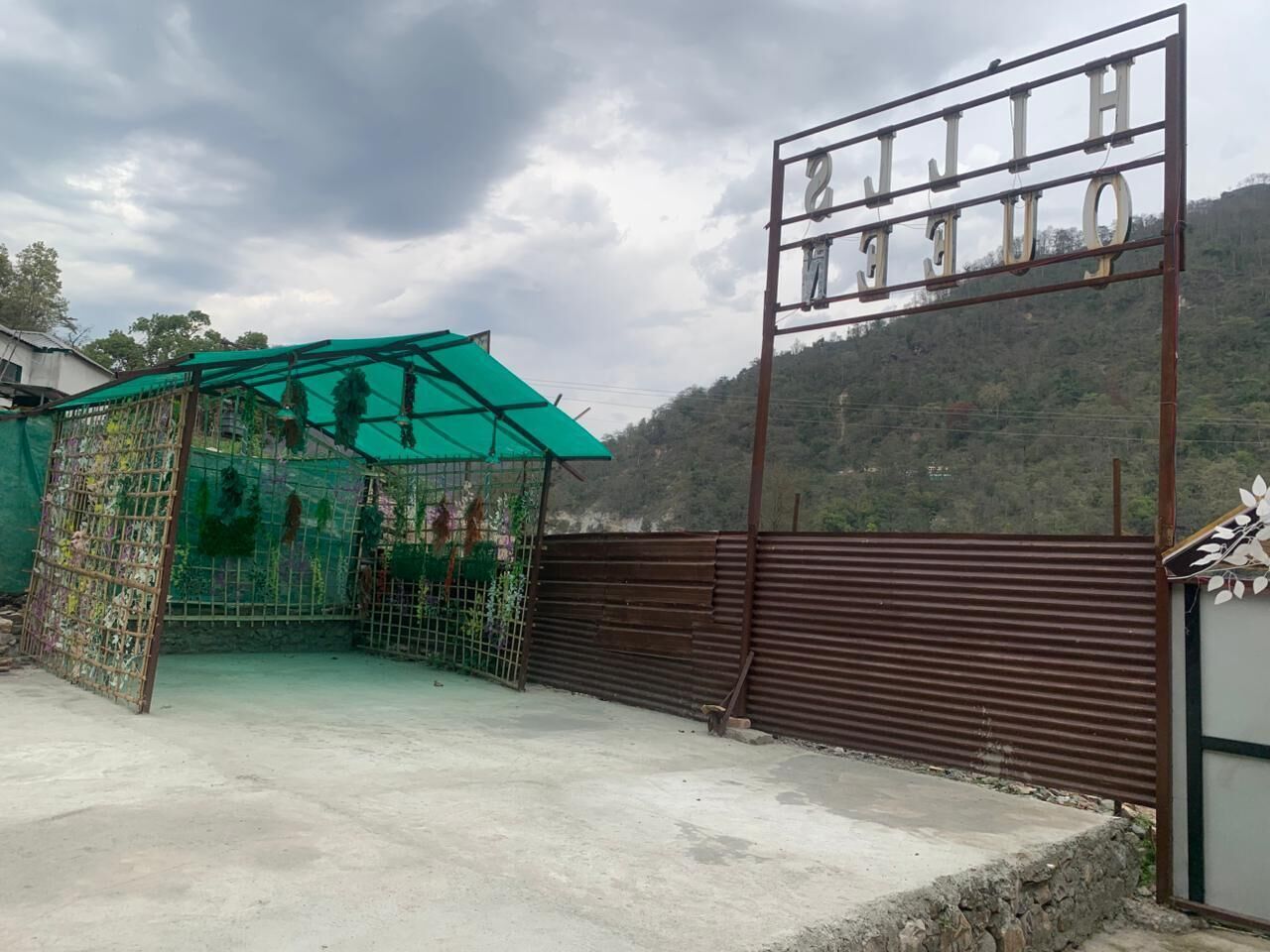 Una entrada protegida por una reja, un letrero metálico, una estructura con techo verde y montañas al fondo.