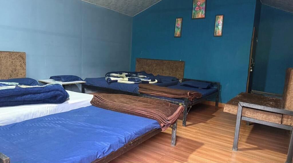A room with three beds, a wooden floor, and a blue wall.