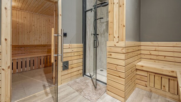A sauna room with wooden benches and a glass-enclosed shower area.
