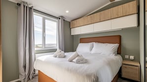 A modern hotel room with a large bed, a wooden headboard, a built-in wardrobe, and a view of the outdoors.