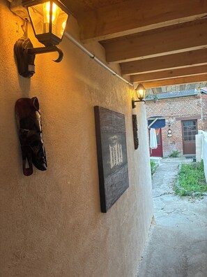 Exterior rústico con techo de viga de madera, una lámpara de pared y un objeto montado que parece una máscara.