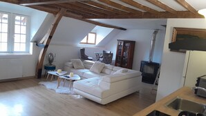 A loft-style living room with a white sofa, wooden beams, a fireplace, and a dining area. - Getaway & wellness accommodation Massage Jacuzzi Sauna (Ravenel)