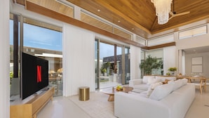 A modern living room with a flat-screen TV, a sofa, a coffee table, and a dining area with a table and chairs. - Luxury 4BR Pool Villa Botanica Prestige (Choeng Thale)