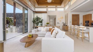 A modern living room with a sofa, coffee table, and a kitchen area with bar stools. - Luxury 4BR Pool Villa Botanica Prestige (Choeng Thale)
