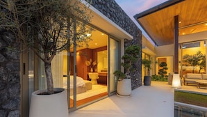A modern house with a stone facade, large windows, and a well-lit interior. - Luxury 4BR Pool Villa Botanica Prestige (Choeng Thale)
