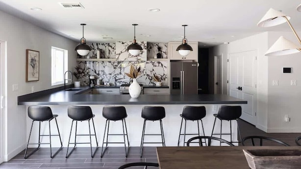Una cocina moderna con salpicadero de mármol, taburetes negros y luminarias colgantes.