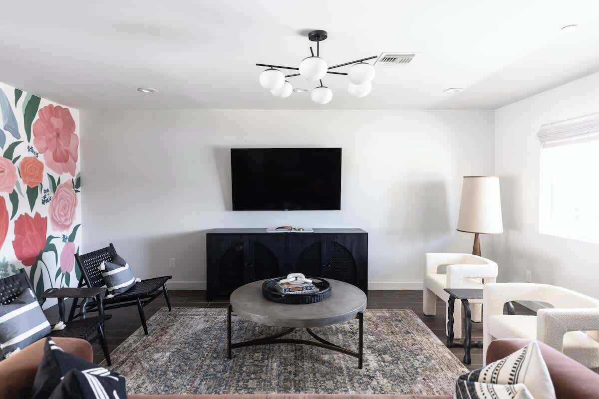 A modern living room with a flat-screen TV, a round coffee table, a black entertainment unit, and a ceiling fan.