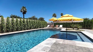 Una piscina con agua cristalina azul, rodeada por un solárium de baldosas y sombrillas amarillas.