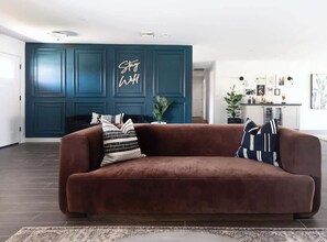 A brown sofa with patterned pillows in a room with teal walls and a 'Stay Well' sign. - Wildflower: New Build, Heated Pool & Dual Masters (Scottsdale)