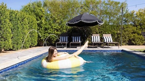Une piscine dans laquelle une personne flotte sur un flotteur gonflable, entourée de chaises longues et d’un parasol.