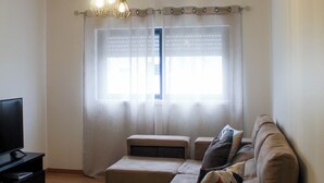 A living room with a sofa, ottoman, TV, and ceiling fan. - Atlantic Central Apartment (Ponta Delgada)