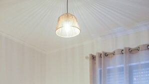 A neatly made bed with folded towels, a bedside lamp, and a hanging light fixture in a room with a window and curtains. - Atlantic Central Apartment (Ponta Delgada)