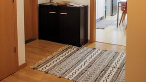 A hallway with a wooden door, a black cabinet, a patterned rug, and a kitchen area with a refrigerator and chairs. - Atlantic Central Apartment (Ponta Delgada)