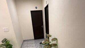 A hallway with a marble floor, a door with a number plate, and potted plants.
