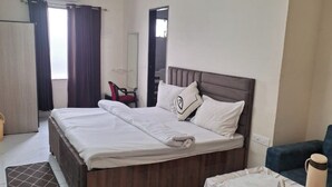 A hotel room with a double bed, a bedside table with a tray, a chair, and a ceiling fan.