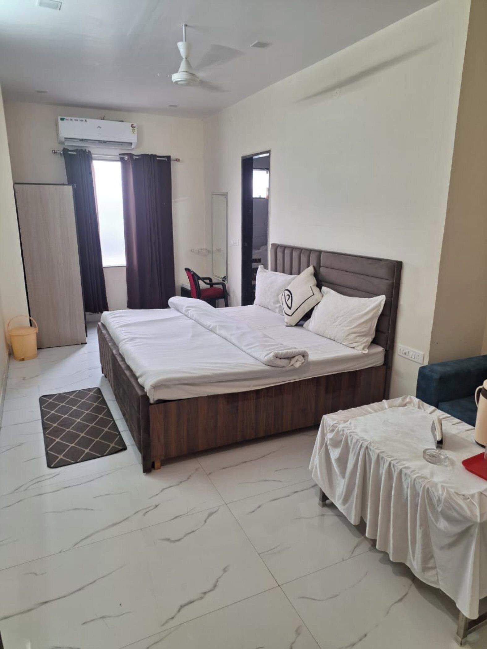A hotel room with a bed, a desk, a chair, a wardrobe, and an air conditioning unit.